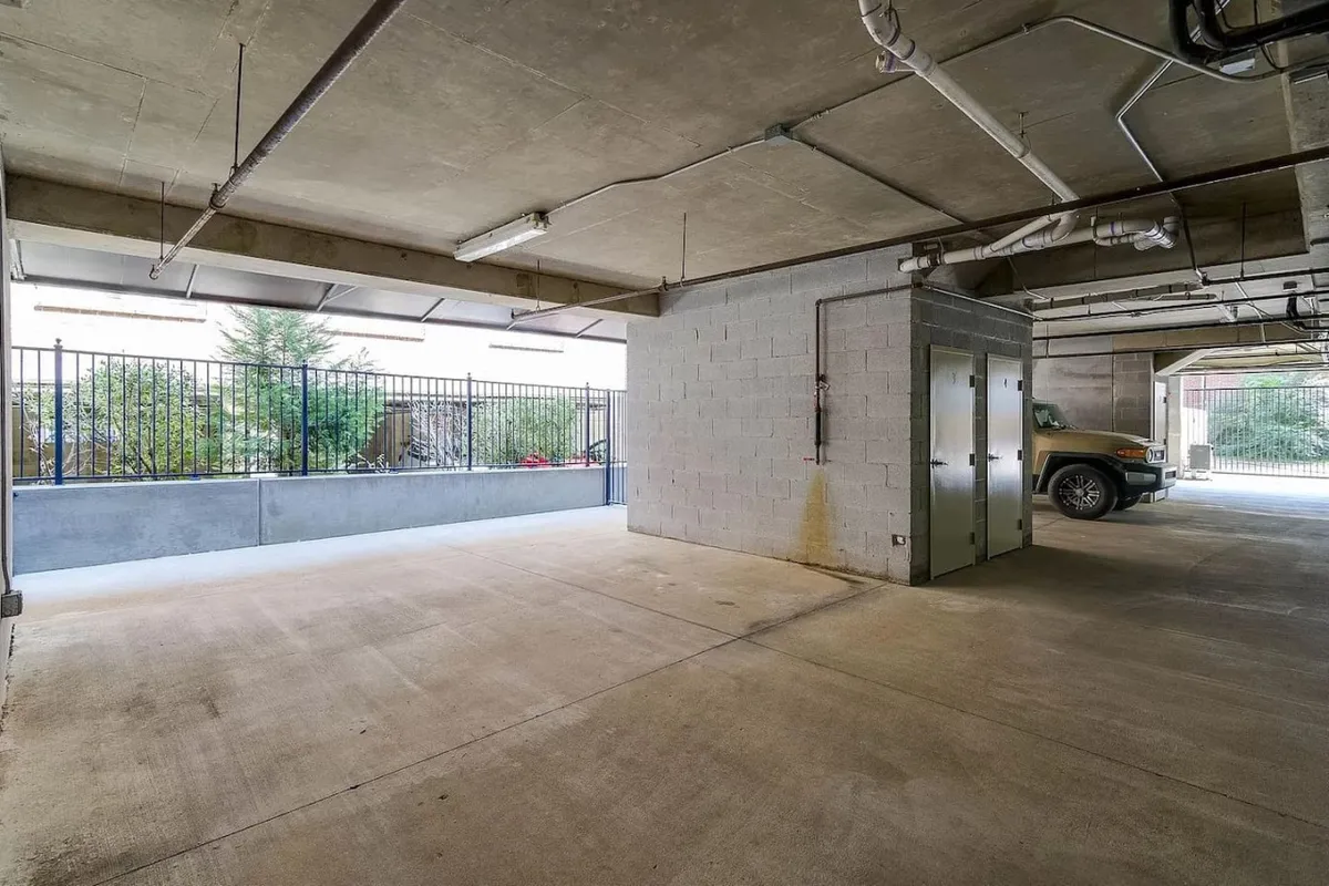This image depicts a practical concrete-walled parking space with a view through the fence to the outdoors. The composition emphasizes convenient, accessible parking and a sense of neighborhood connection beyond the property.