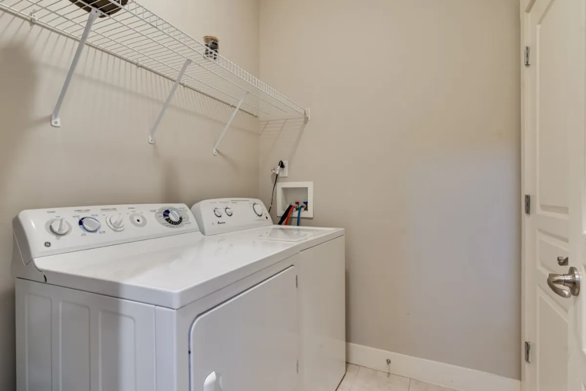 A bright laundry area equipped with a washing machine, dryer, and overhead shelving for storage. The space is clean, organized, and practical.