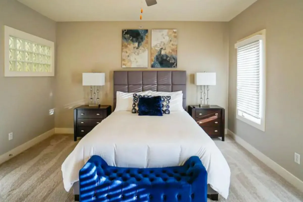A tranquil bedroom featuring a plush bed, elegant artwork above the headboard, a well-appointed nightstand, and a bench at the foot of the bed. The atmosphere is peaceful and inviting, ideal for restful nights or quiet reading.