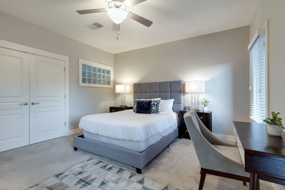 An inviting upstairs bedroom that seamlessly incorporates a desk area. The space features a cozy bed, nightstands, decorative artwork, and a window letting in natural light. The desk is positioned for both work and relaxation, suggesting a smooth transition between productivity and downtime.
